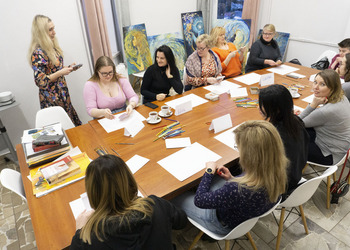 Grupa kobiet przy stole. Przed nimi przybory do malowania